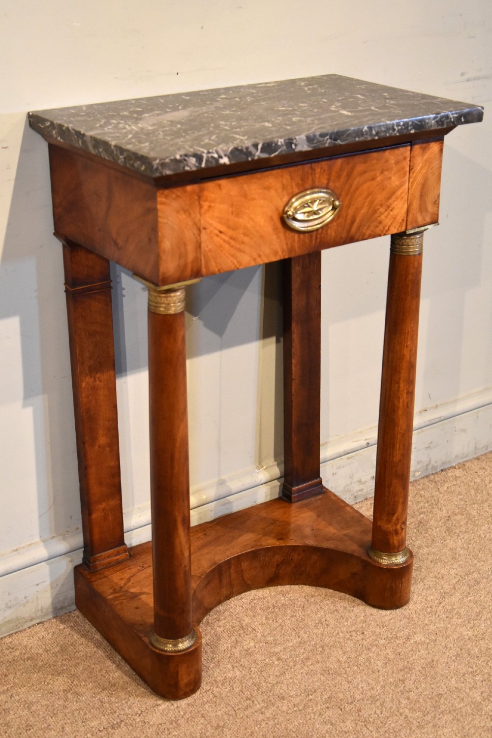 A French Empire flame mahogany console table featuring a grey speckled marble top, a single frieze drawer, and cylindrical column front legs on a shaped base. View II