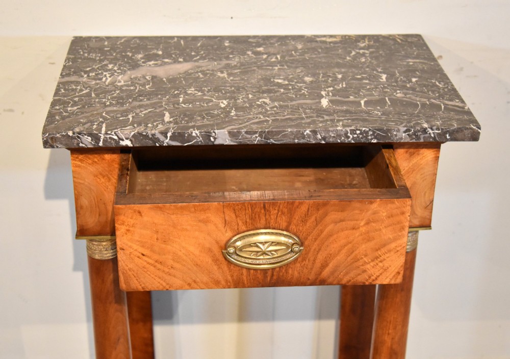A French Empire flame mahogany console table featuring a grey speckled marble top, a single frieze drawer, and cylindrical column front legs on a shaped base. View III