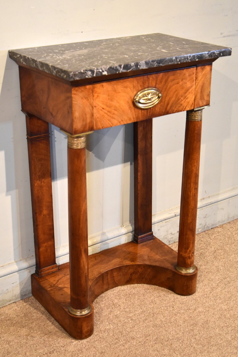 A French Empire flame mahogany console table featuring a grey speckled marble top, a single frieze drawer, and cylindrical column front legs on a shaped base. View IV