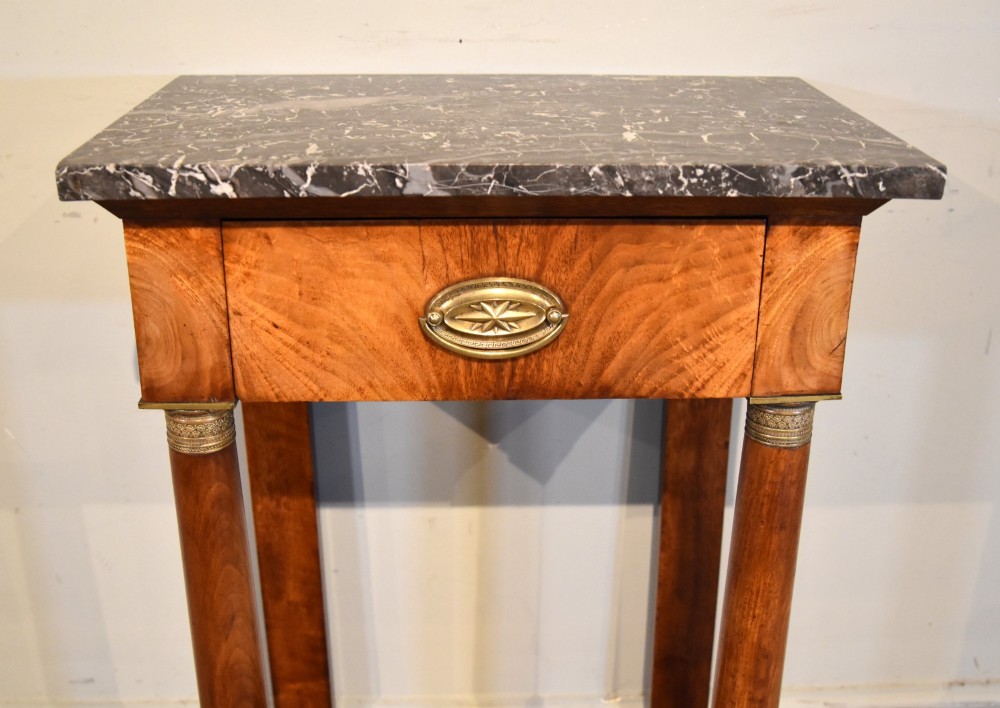 A French Empire flame mahogany console table featuring a grey speckled marble top, a single frieze drawer, and cylindrical column front legs on a shaped base. View VI
