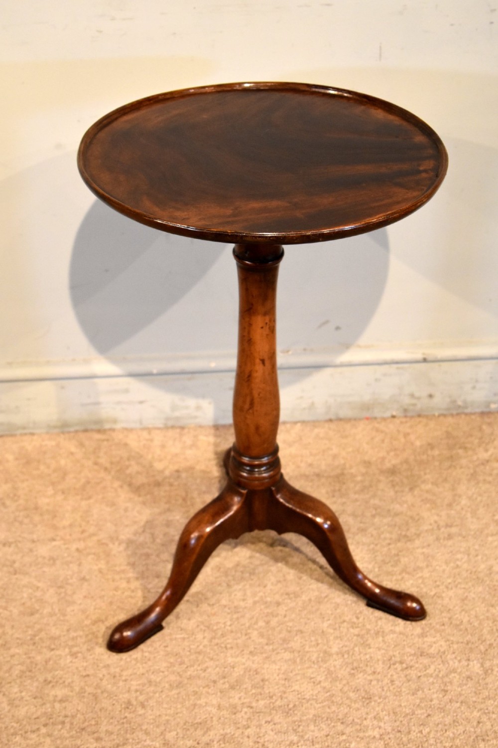 A George III mahogany tripod table featuring a circular dish top supported on a turned baluster column with three splayed legs.