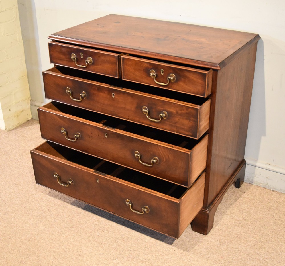 An 18th-century Georgian mahogany chest of drawers featuring two short over three long graduated drawers, brass swan-neck handles, keyhole escutcheons, and bracket feet. View IV