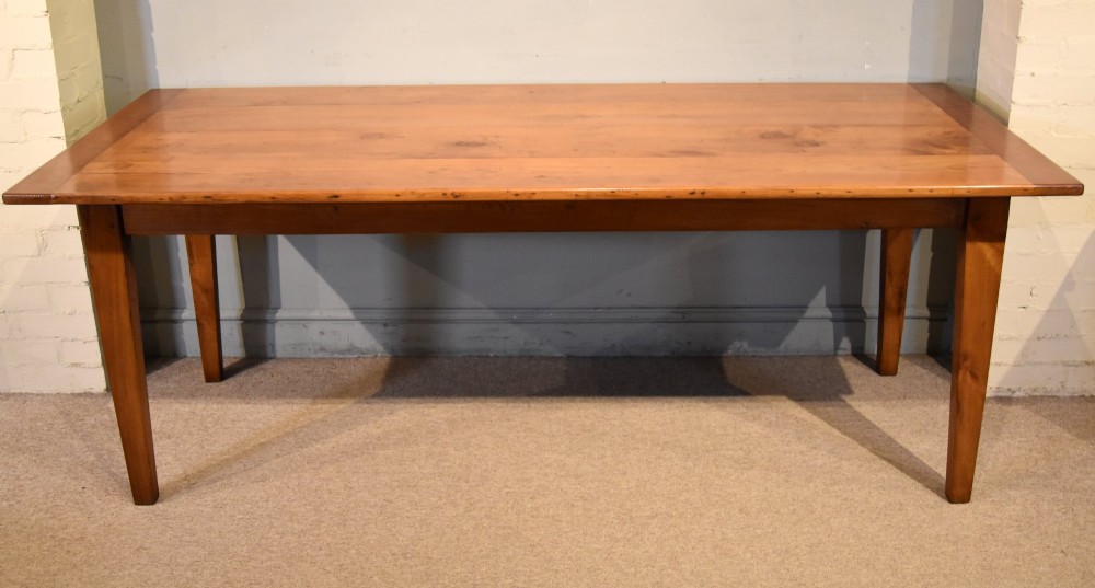 A nineteenth-century French cherry wood farmhouse table featuring a rectangular planked top, breadboard ends, a simple apron, and square tapered legs.