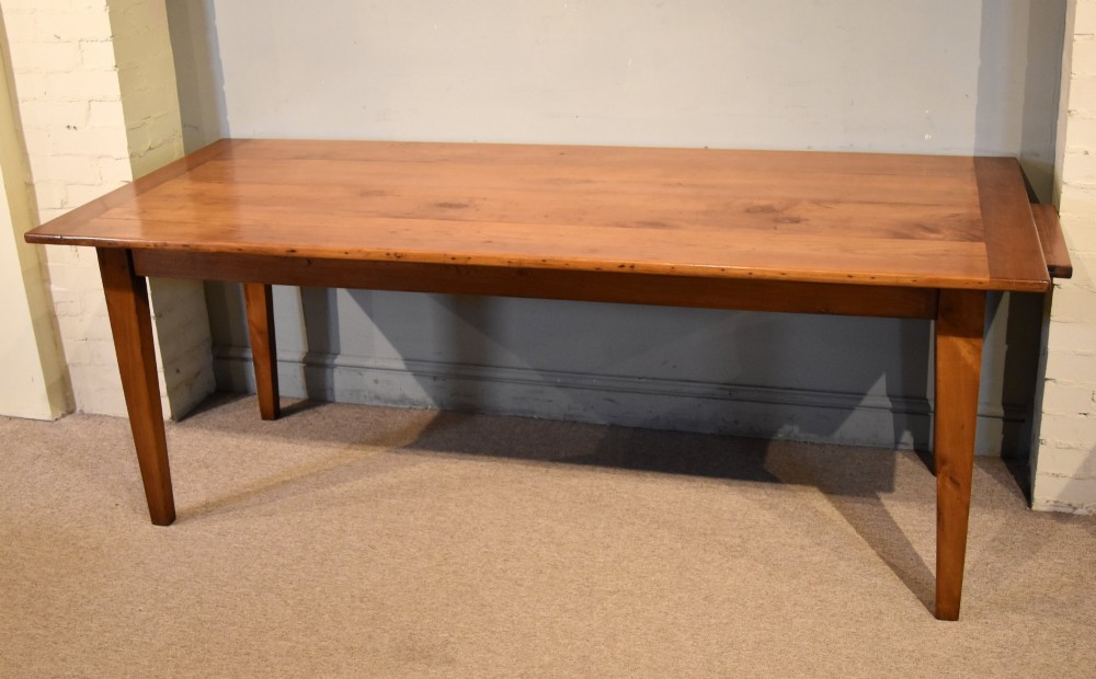 A nineteenth-century French cherry wood farmhouse table featuring a rectangular planked top, breadboard ends, a simple apron, and square tapered legs. View II