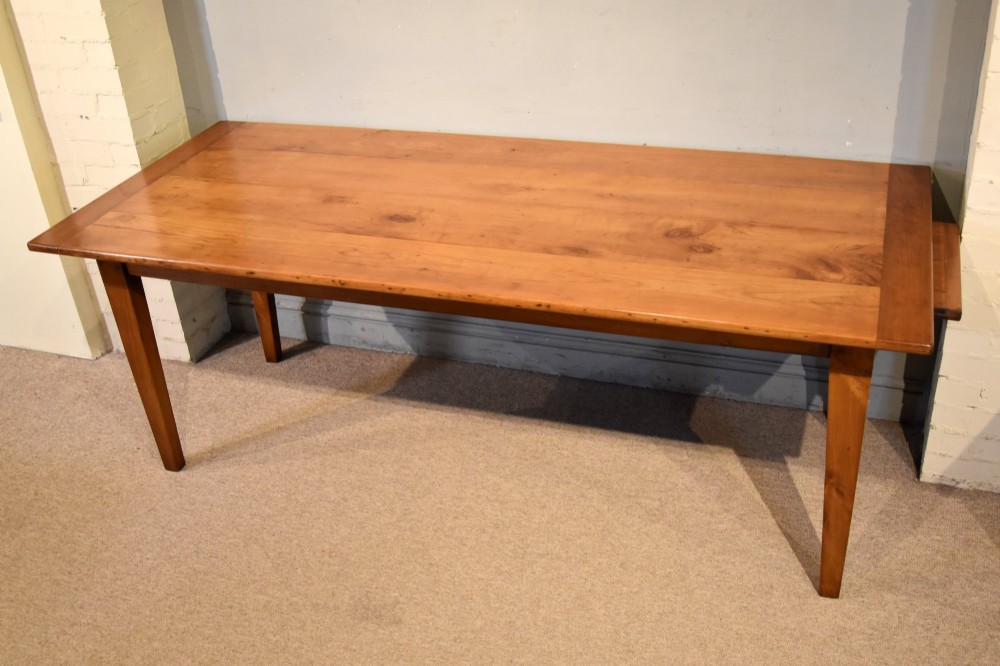 A nineteenth-century French cherry wood farmhouse table featuring a rectangular planked top, breadboard ends, a simple apron, and square tapered legs. View III