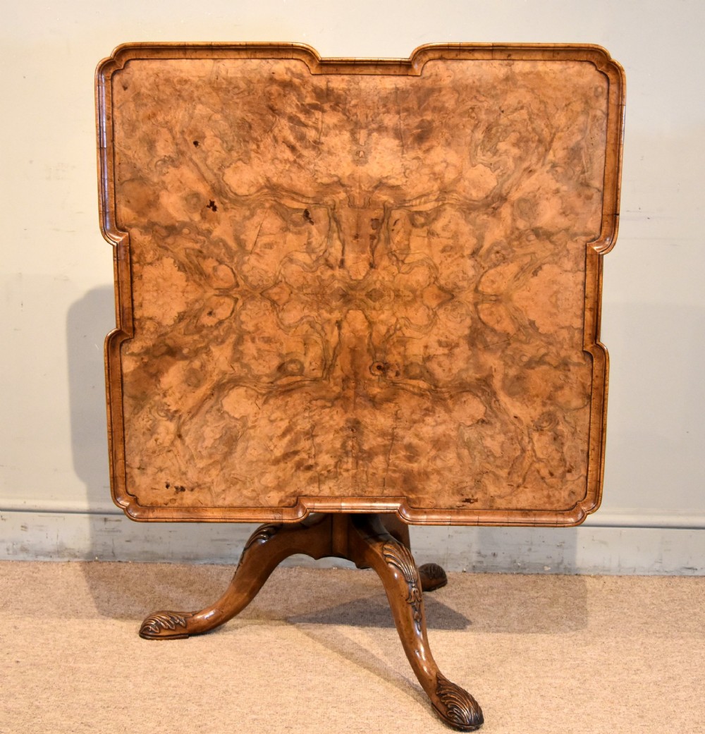 A Victorian tilt-top supper table made from burr walnut featuring a shaped top and a carved tripod pedestal base.