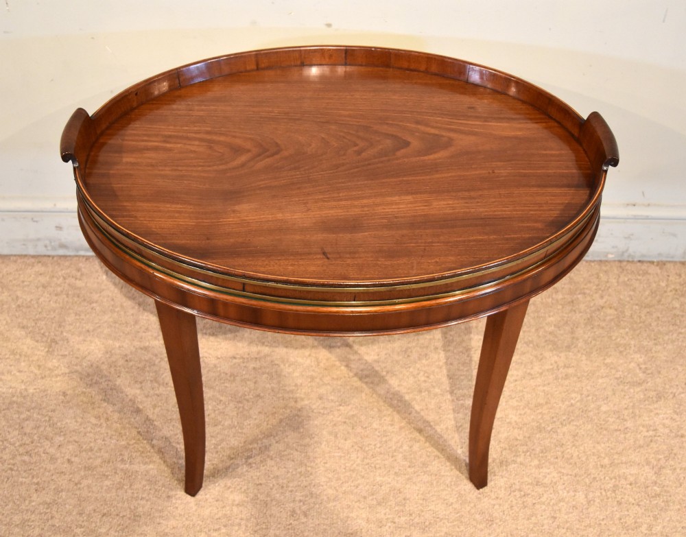 A late eighteenth-century oval mahogany tray table featuring a raised gallery edge, side cut-out handles, brass rim detailing, and tapered curved legs.