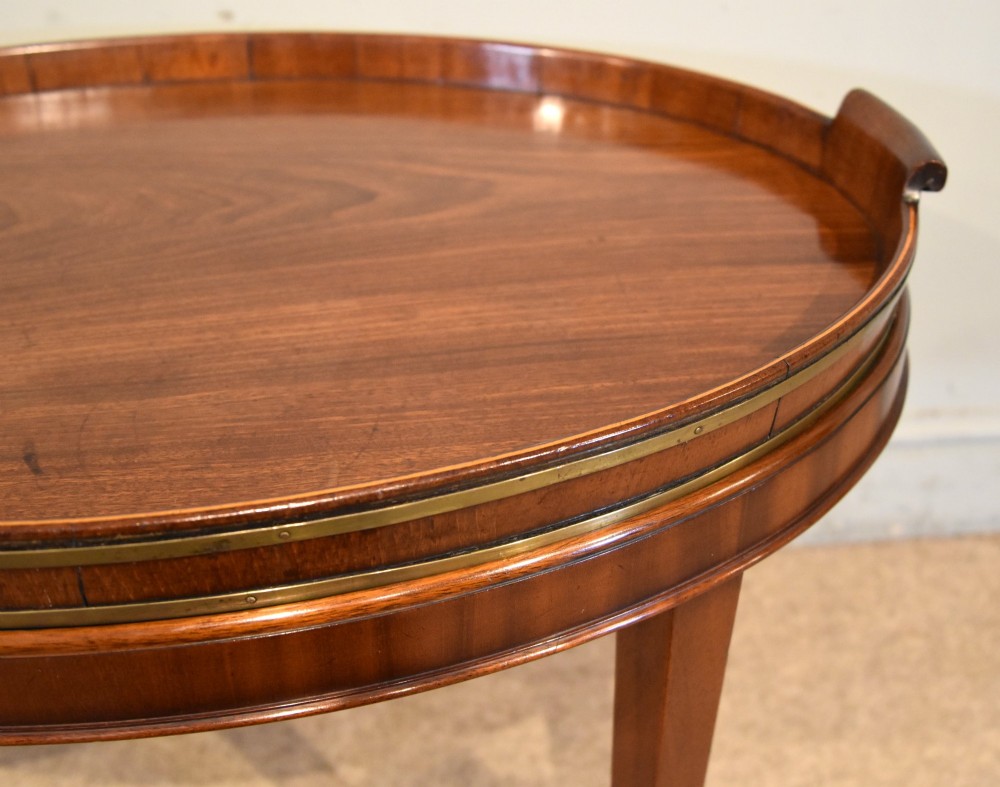 A late eighteenth-century oval mahogany tray table featuring a raised gallery edge, side cut-out handles, brass rim detailing, and tapered curved legs. View V