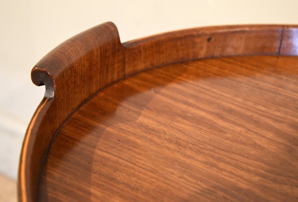 A late eighteenth-century oval mahogany tray table featuring a raised gallery edge, side cut-out handles, brass rim detailing, and tapered curved legs. View VII