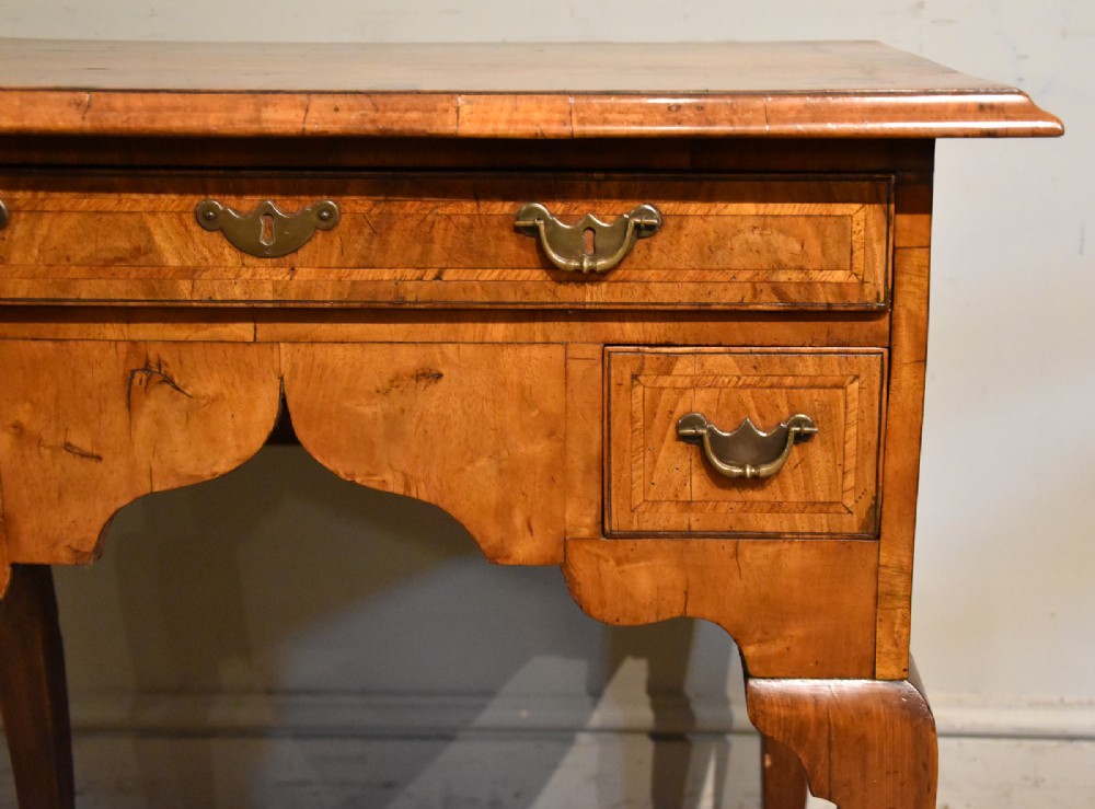 An 18th-century walnut lowboy featuring a crossbanded top, three drawers with brass drop handles, a shaped apron, and four cabriole legs. View V