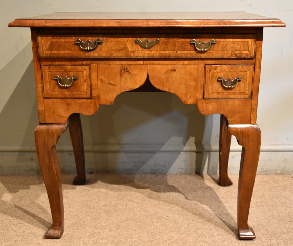 An 18th-century walnut lowboy featuring a crossbanded top, three drawers with brass drop handles, a shaped apron, and four cabriole legs.