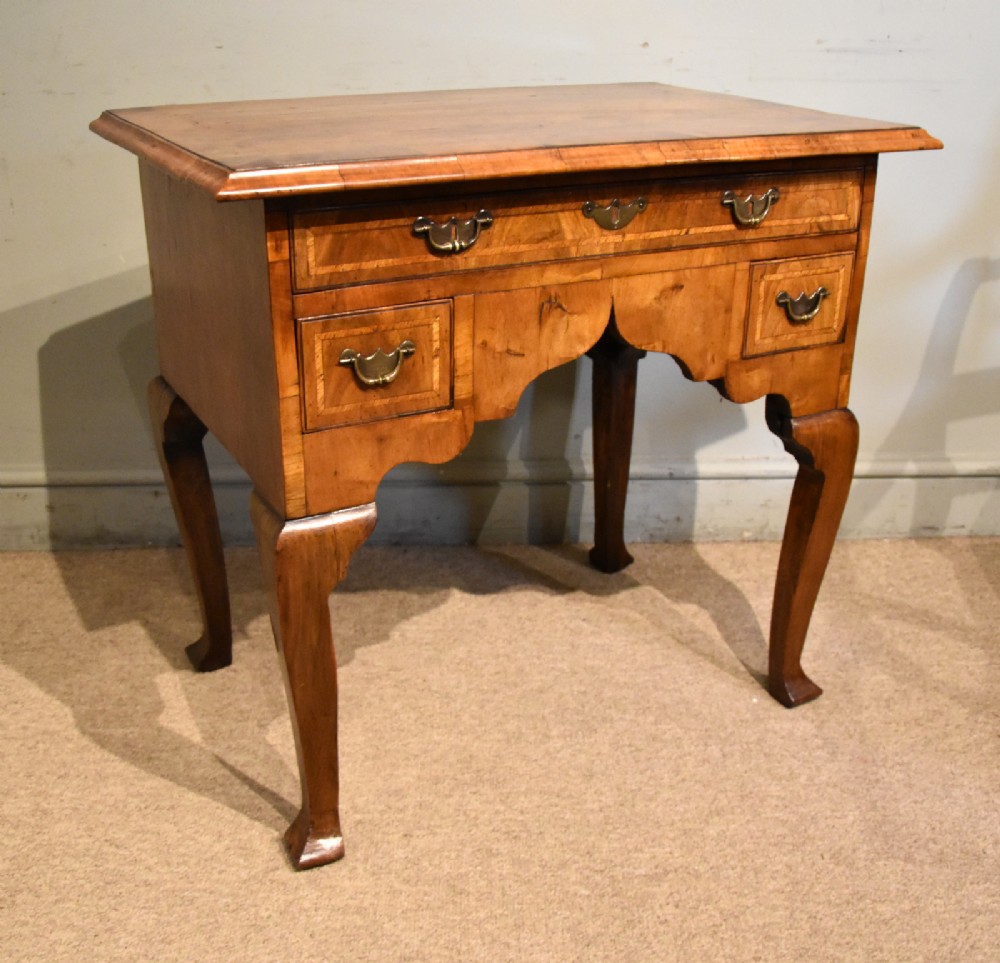 An 18th-century walnut lowboy featuring a crossbanded top, three drawers with brass drop handles, a shaped apron, and four cabriole legs. View VI