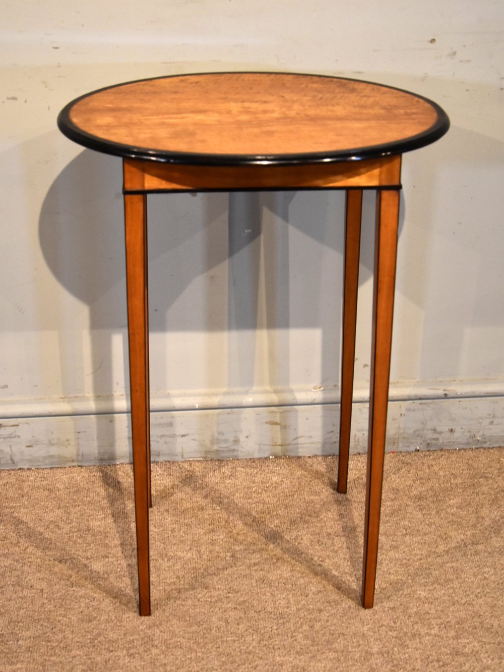 A late 18th-century oval satinwood occasional table featuring a dark banded top border and slender square tapered legs.