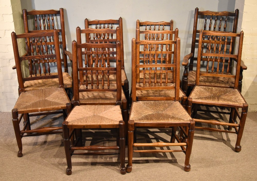 A set of ten brown oak dining chairs featuring double-tier spindle backs, woven rush seats, and turned stretchers.