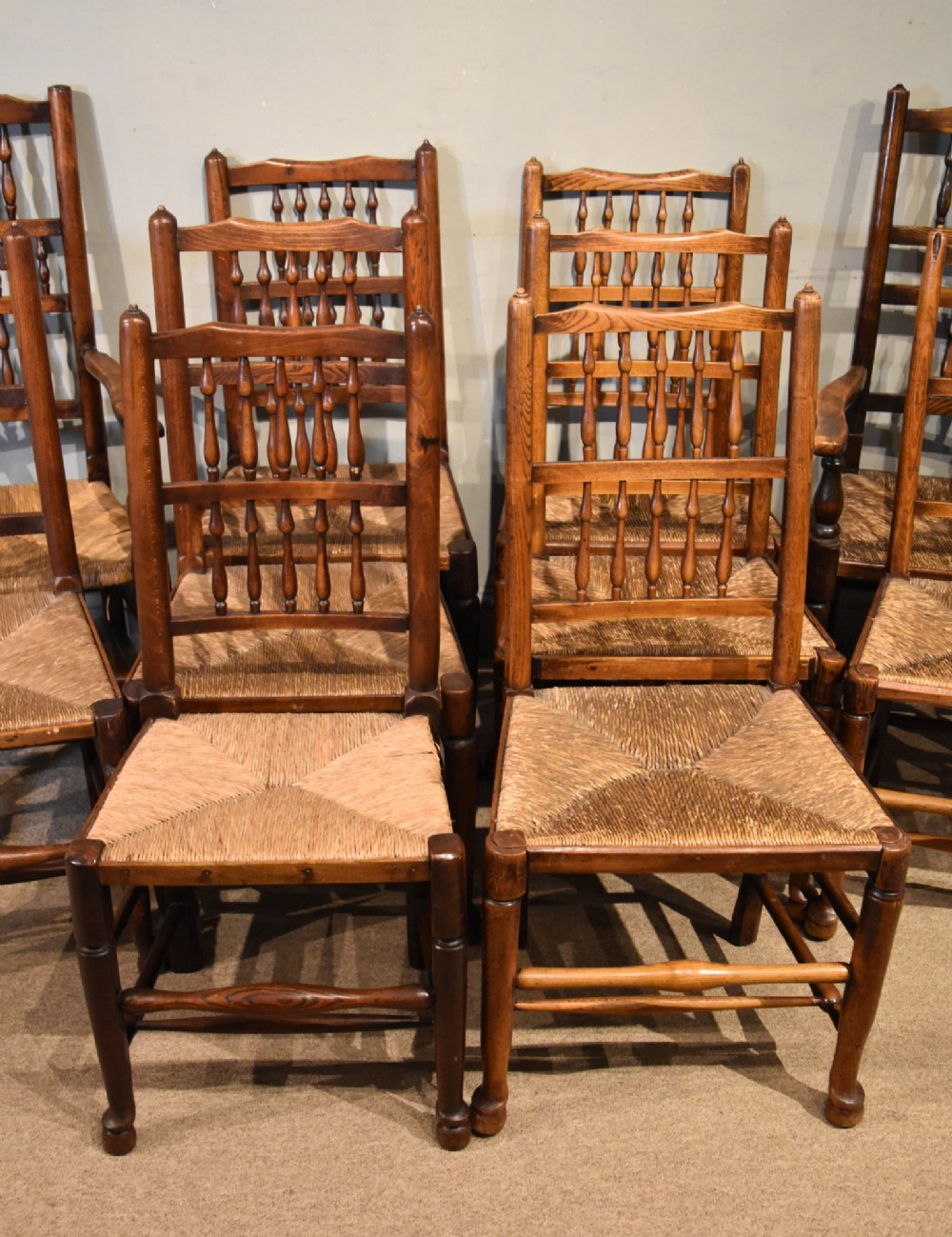 A set of ten brown oak dining chairs featuring double-tier spindle backs, woven rush seats, and turned stretchers. View II