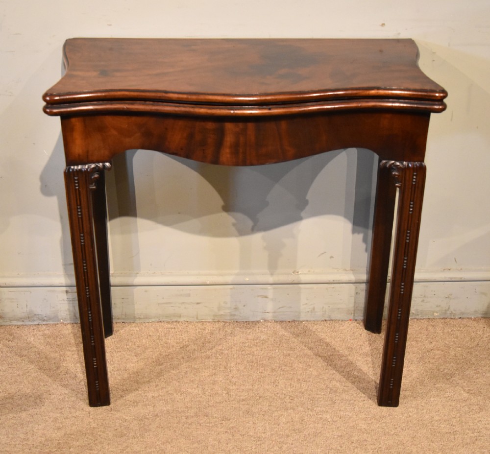 A George III Cuban mahogany fold-over tea table featuring a serpentine front, carved corner brackets, and fluted legs.