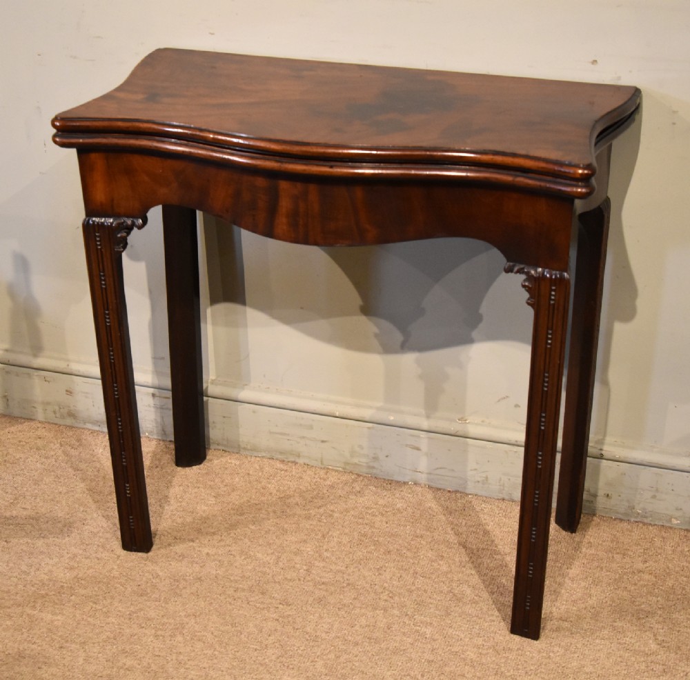 A George III Cuban mahogany fold-over tea table featuring a serpentine front, carved corner brackets, and fluted legs. View II