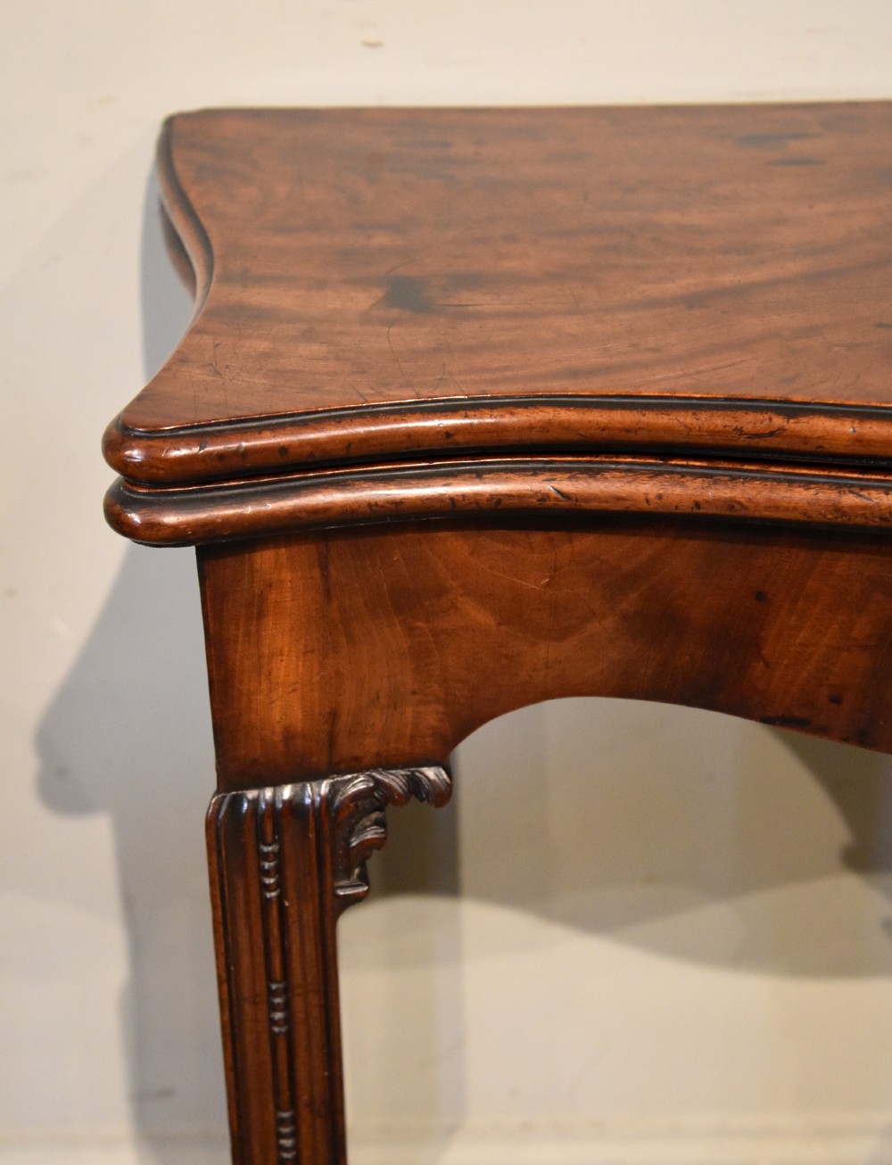 A George III Cuban mahogany fold-over tea table featuring a serpentine front, carved corner brackets, and fluted legs. View IV