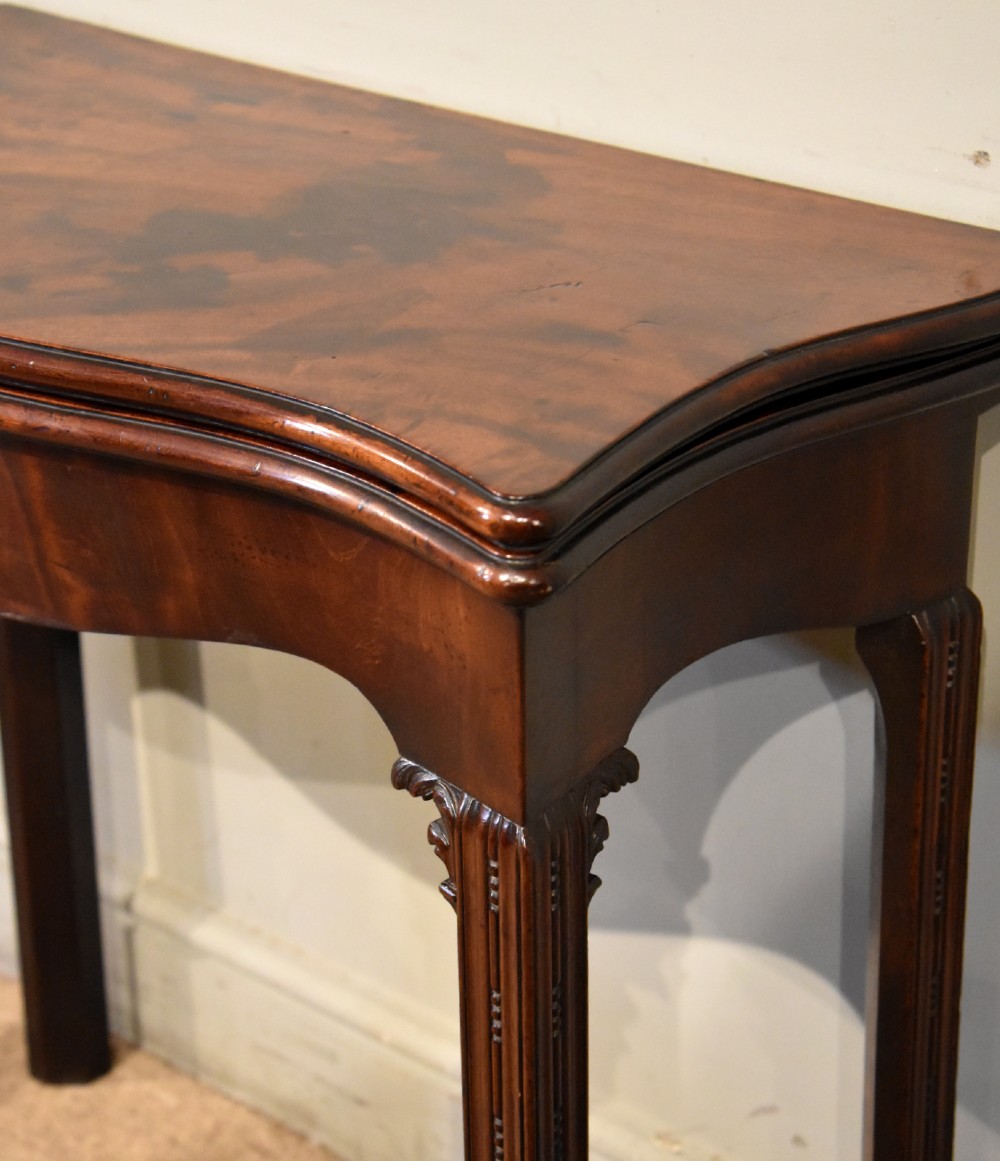 A George III Cuban mahogany fold-over tea table featuring a serpentine front, carved corner brackets, and fluted legs. View V