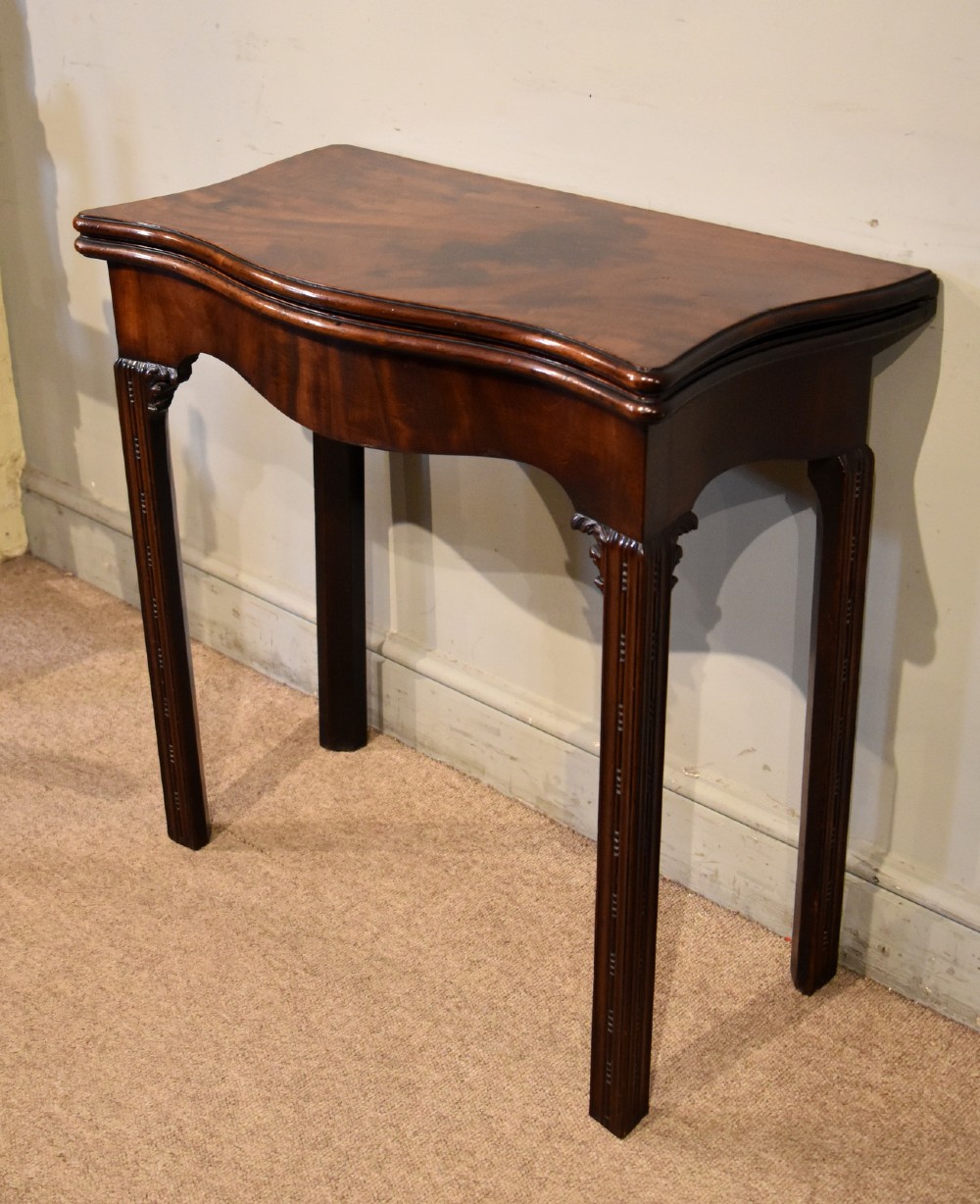 A George III Cuban mahogany fold-over tea table featuring a serpentine front, carved corner brackets, and fluted legs. View VI