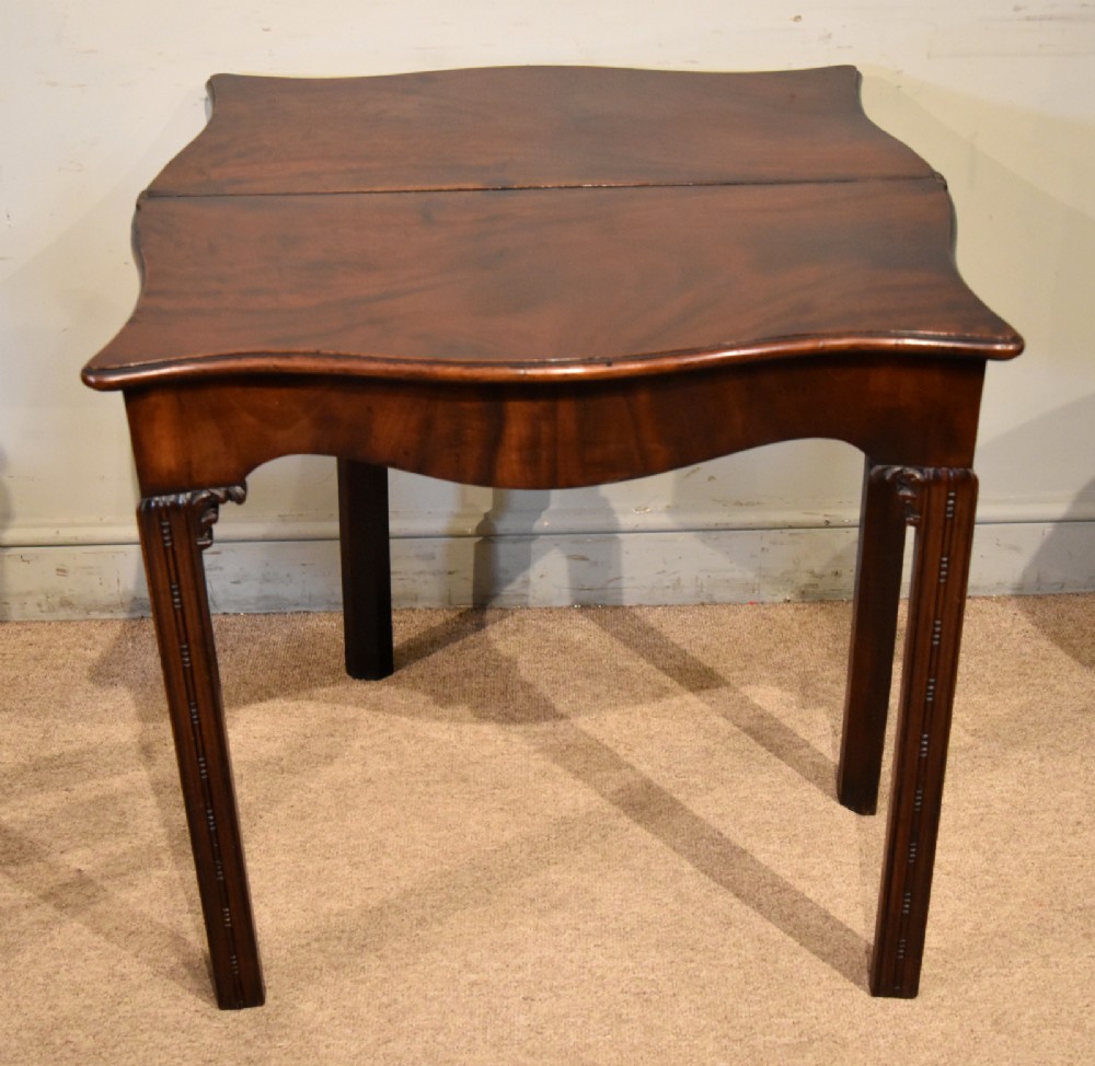 A George III Cuban mahogany fold-over tea table featuring a serpentine front, carved corner brackets, and fluted legs. View VII