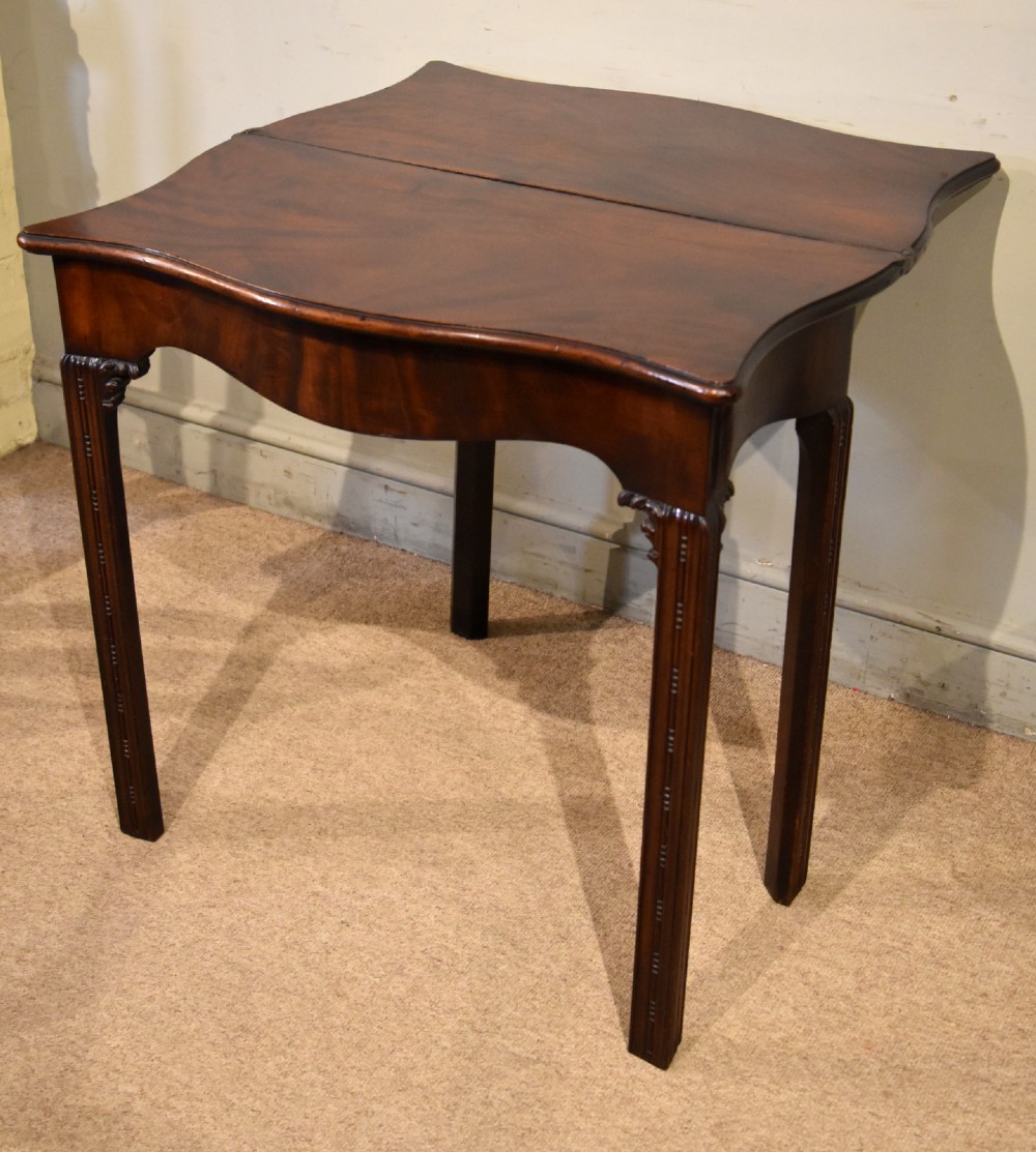 A George III Cuban mahogany fold-over tea table featuring a serpentine front, carved corner brackets, and fluted legs. View VIII