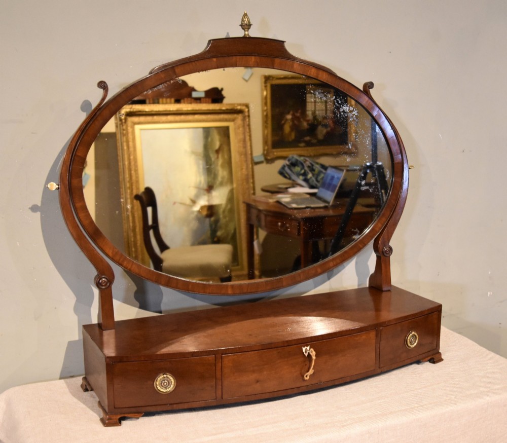 A Regency mahogany bowfronted dressing mirror with an oval swivelling mirror plate, brass finial, and a three-drawer base with brass handles.