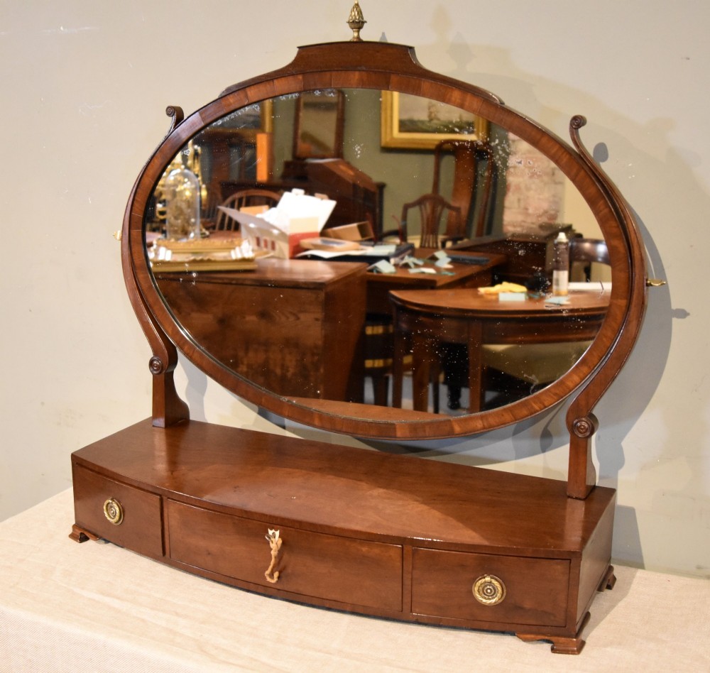 A Regency mahogany bowfronted dressing mirror with an oval swivelling mirror plate, brass finial, and a three-drawer base with brass handles. View III