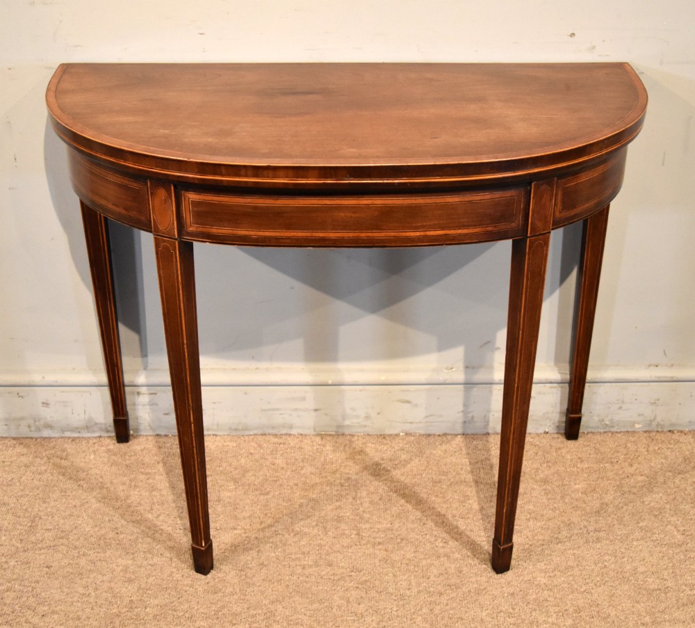 A George III mahogany demi-lune card table featuring boxwood stringing inlay and square tapered legs.