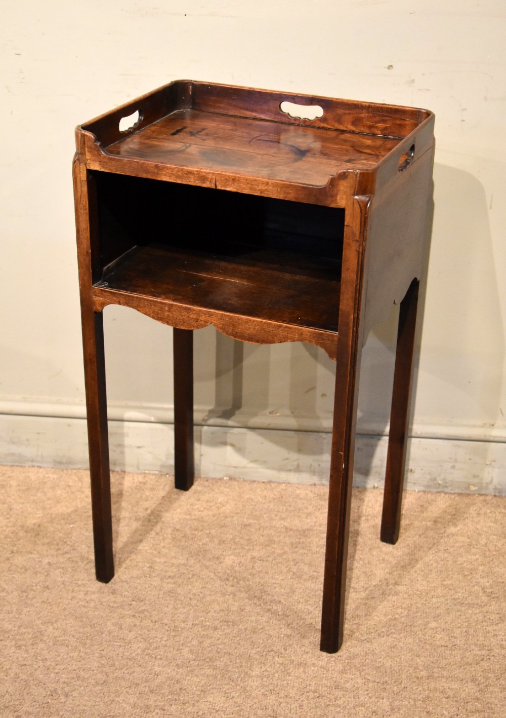 A George III mahogany pot cupboard featuring a gallery tray top with cut-out handles, an open storage shelf, and square straight legs.