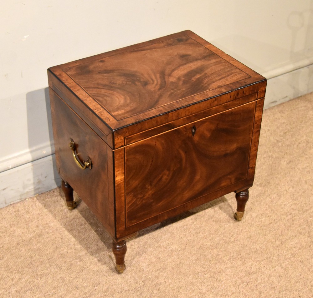 A Regency mahogany cellerette featuring flame timber veneers, crossbanded borders, a central keyhole, and turned legs on brass castors. View II