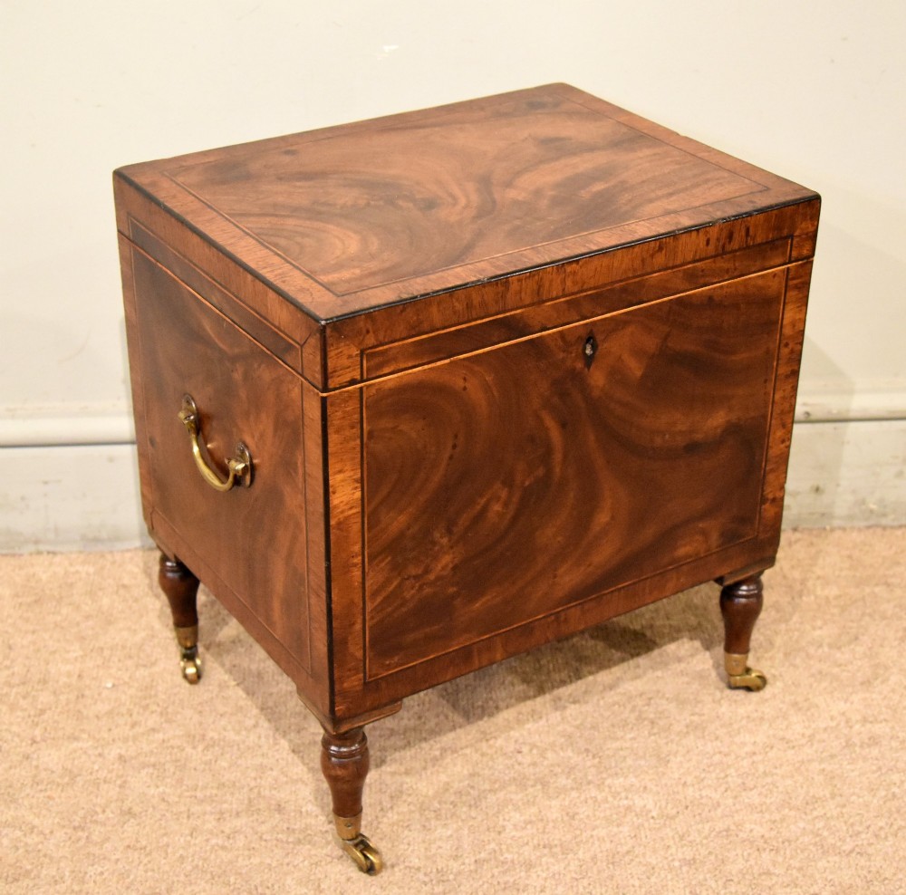 A Regency mahogany cellerette featuring flame timber veneers, crossbanded borders, a central keyhole, and turned legs on brass castors. View VI