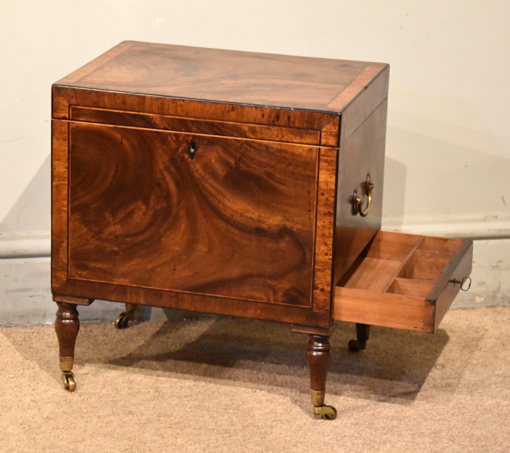 A Regency mahogany cellerette featuring flame timber veneers, crossbanded borders, a central keyhole, and turned legs on brass castors. View VII