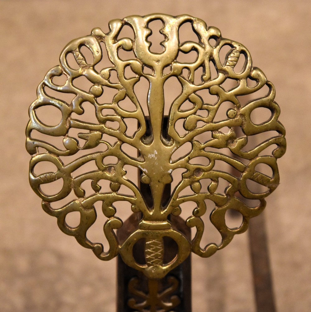 A pair of 19th-century brass and cast iron fire dogs featuring pierced circular foliate brass finials on dark iron uprights with horizontal log billets. View V