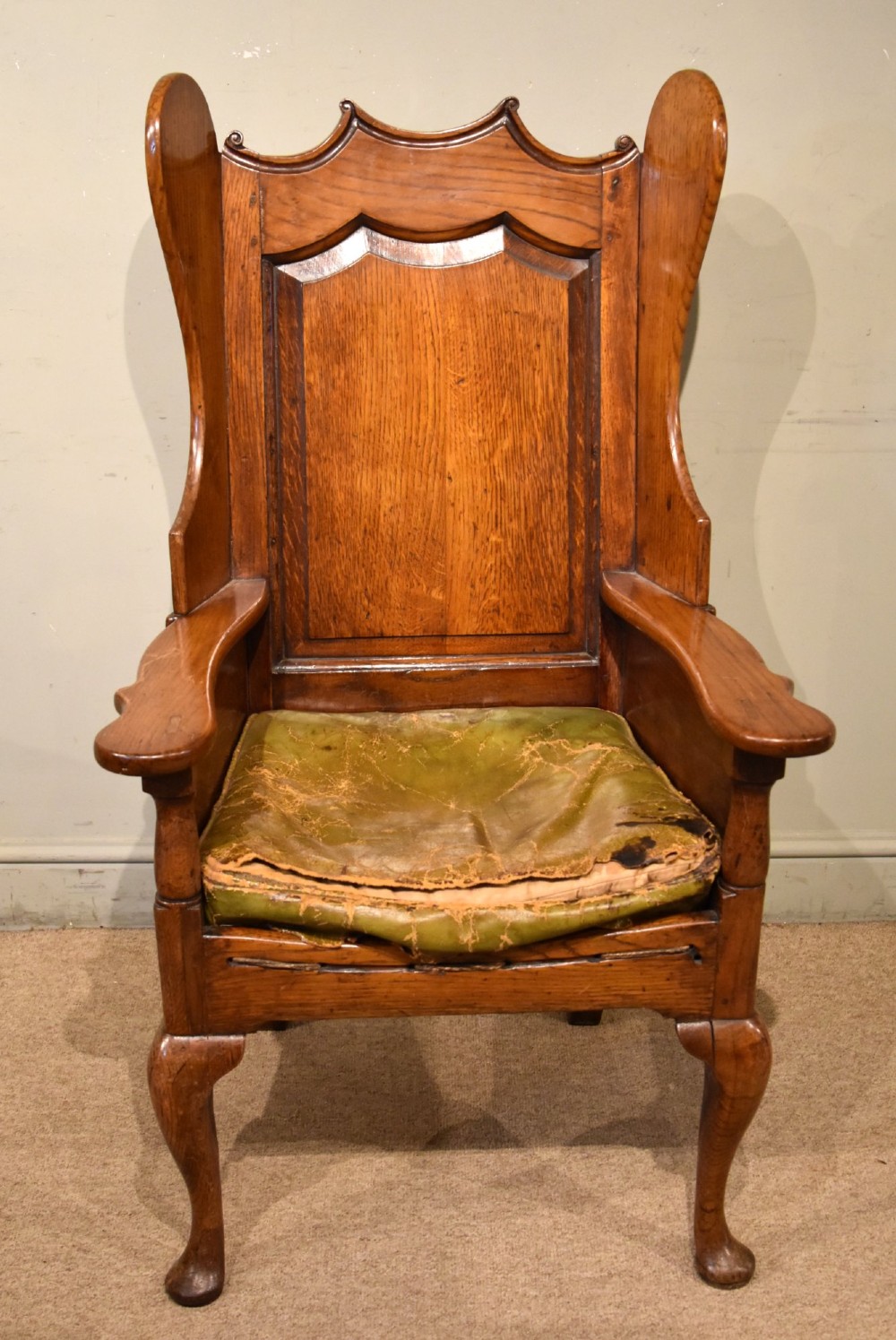 An 18th-century solid oak wingback armchair with a fielded panel back, shaped wings, cabriole front legs, and an aged green cushion. View II