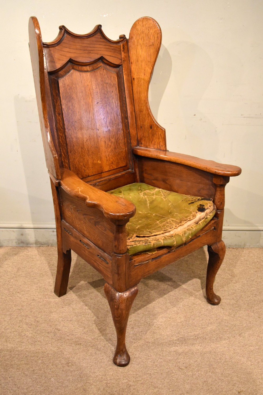 An 18th-century solid oak wingback armchair with a fielded panel back, shaped wings, cabriole front legs, and an aged green cushion. View III