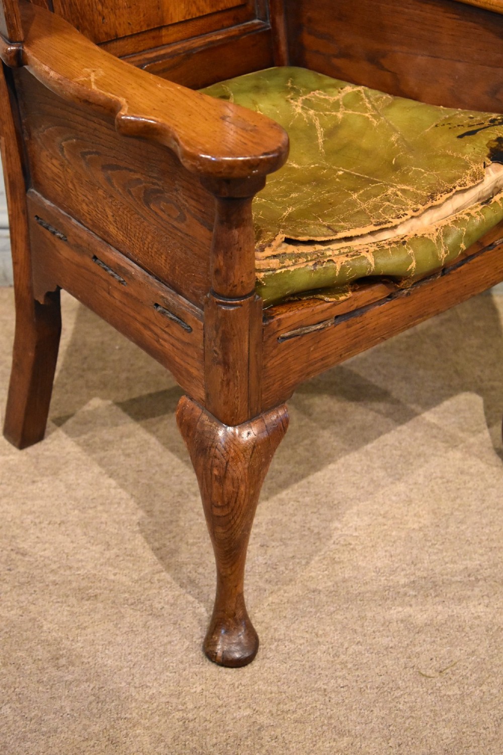 An 18th-century solid oak wingback armchair with a fielded panel back, shaped wings, cabriole front legs, and an aged green cushion. View IV