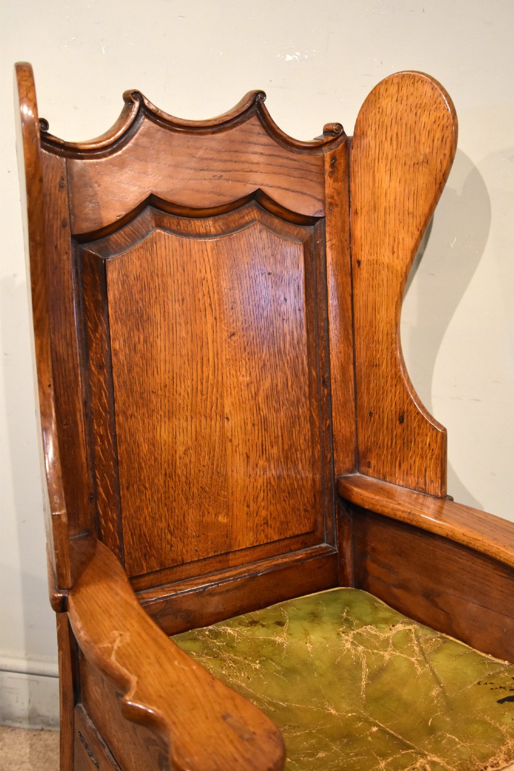 An 18th-century solid oak wingback armchair with a fielded panel back, shaped wings, cabriole front legs, and an aged green cushion. View V
