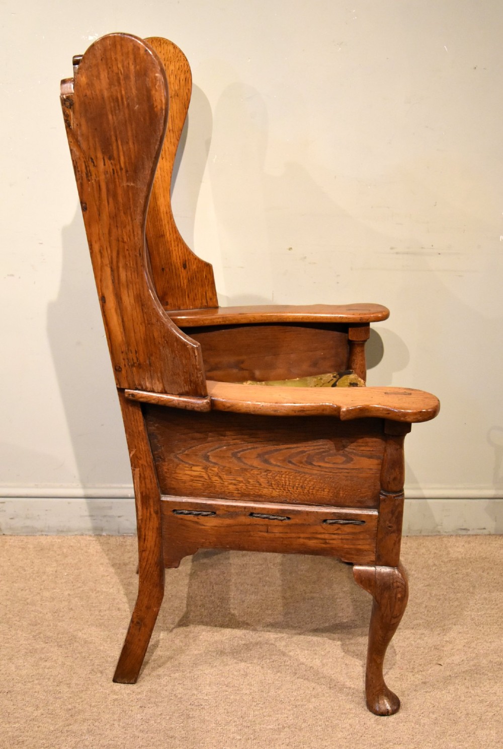 An 18th-century solid oak wingback armchair with a fielded panel back, shaped wings, cabriole front legs, and an aged green cushion. View VI