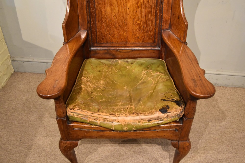 An 18th-century solid oak wingback armchair with a fielded panel back, shaped wings, cabriole front legs, and an aged green cushion. View VIII