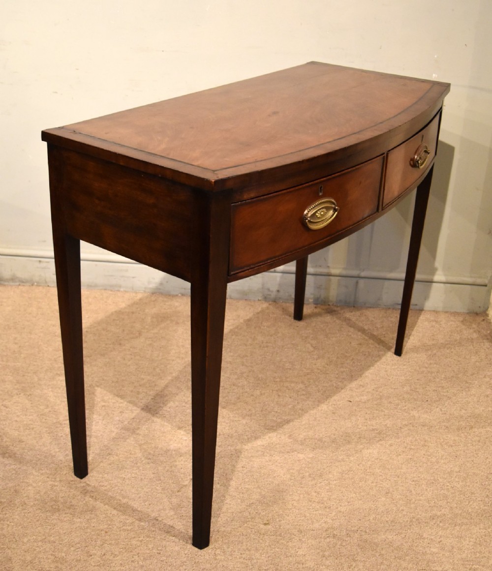 A George III bowfront mahogany serving table featuring two drawers with brass oval handles and slender tapered legs. View VI