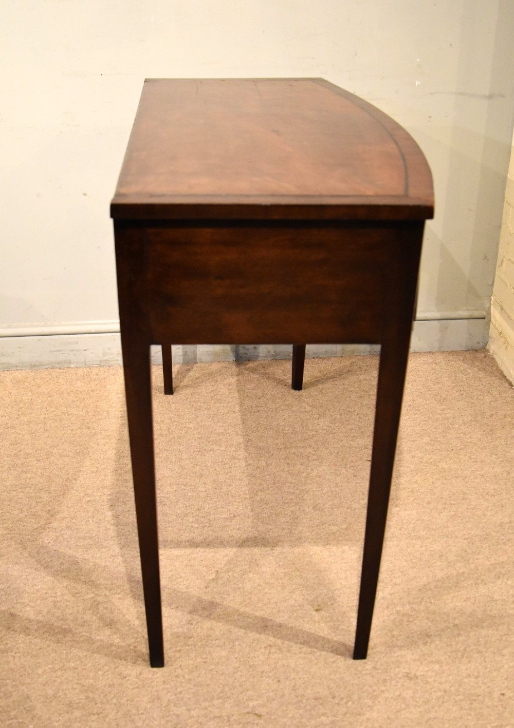 A George III bowfront mahogany serving table featuring two drawers with brass oval handles and slender tapered legs. View VII