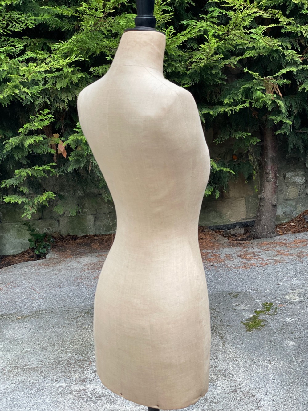A fabric-covered female tailors dummy torso featuring stitched neutral linen upholstery and a dark turned neck finial.