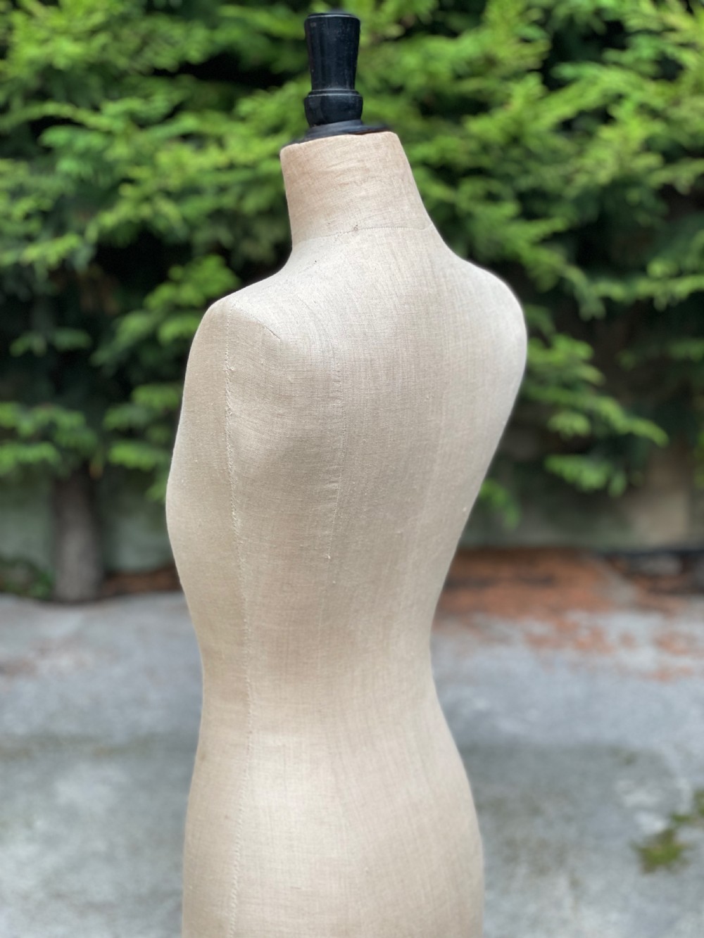 A fabric-covered female tailors dummy torso featuring stitched neutral linen upholstery and a dark turned neck finial. View X