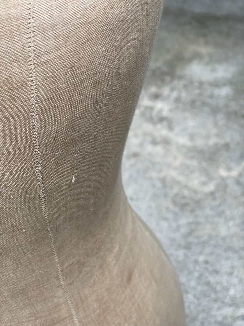 A fabric-covered female tailors dummy torso featuring stitched neutral linen upholstery and a dark turned neck finial. View XV