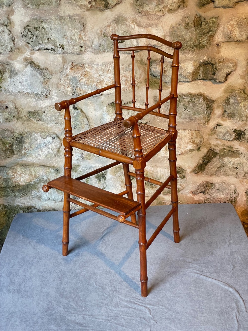 An antique Victorian faux bamboo turned wood childs high chair featuring a woven cane seat and integrated footrest.