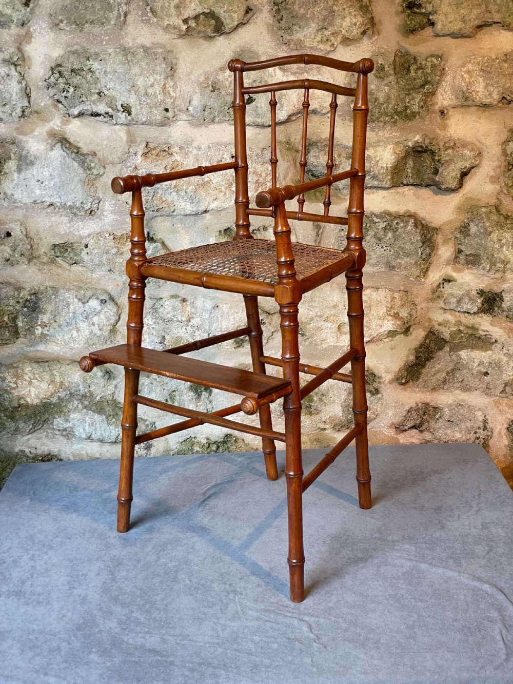 An antique Victorian faux bamboo turned wood childs high chair featuring a woven cane seat and integrated footrest. View II