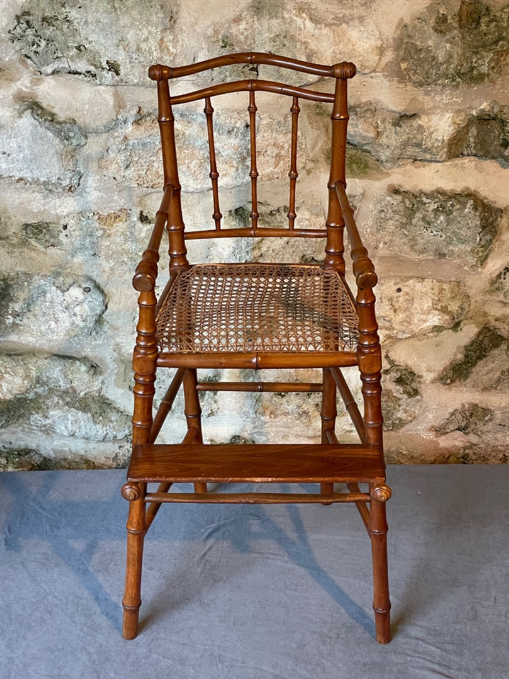 An antique Victorian faux bamboo turned wood childs high chair featuring a woven cane seat and integrated footrest. View III