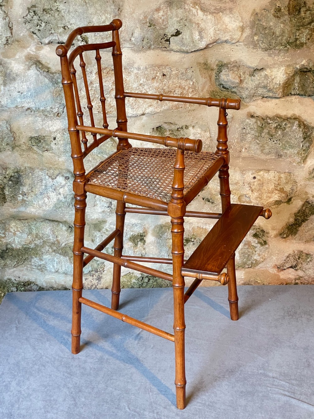An antique Victorian faux bamboo turned wood childs high chair featuring a woven cane seat and integrated footrest. View IV