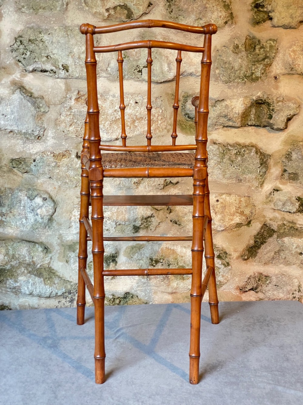 An antique Victorian faux bamboo turned wood childs high chair featuring a woven cane seat and integrated footrest. View XVI